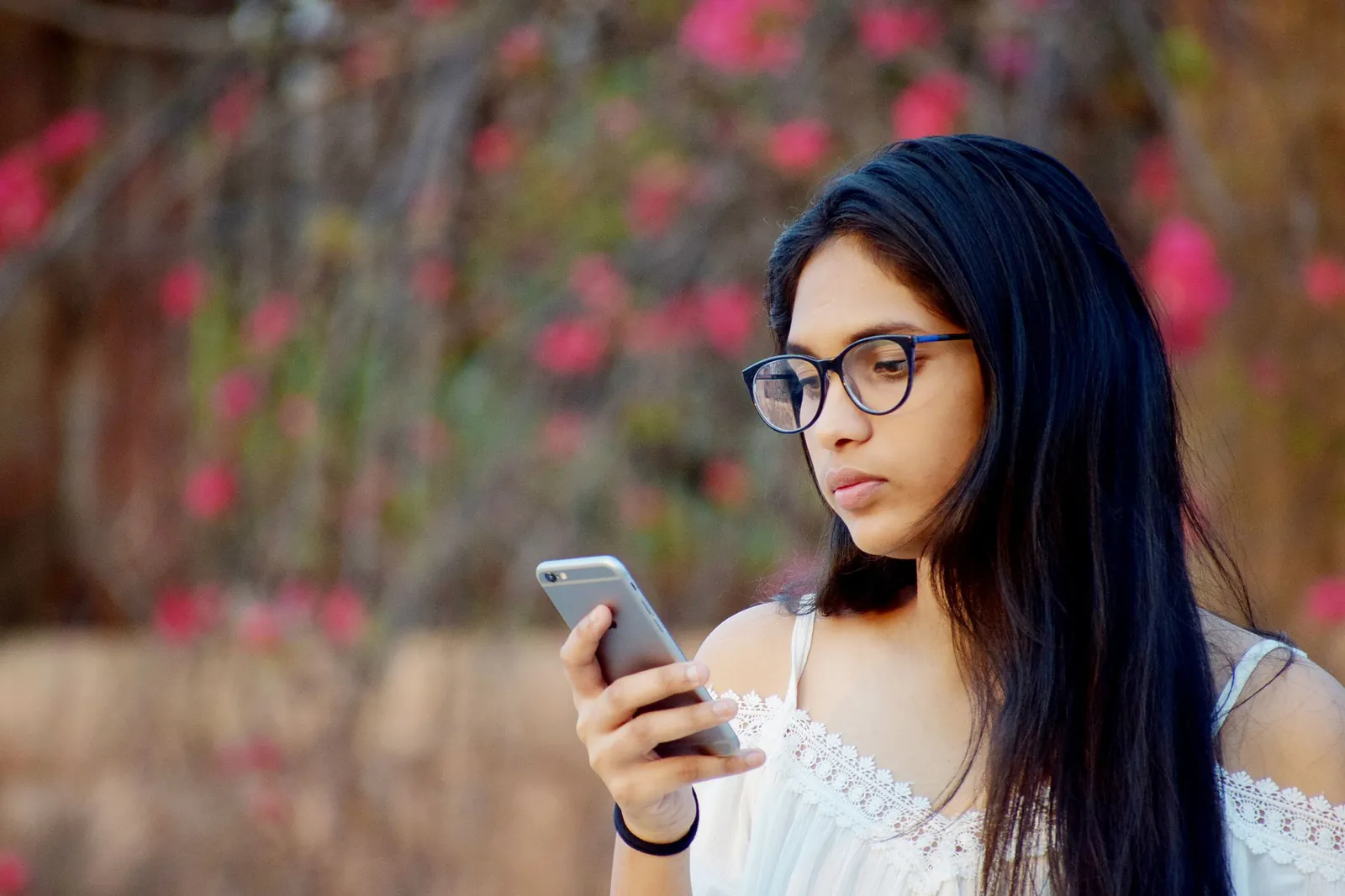 A young Malayali woman looking at her phone, thinking about reaching out to a psychologist
