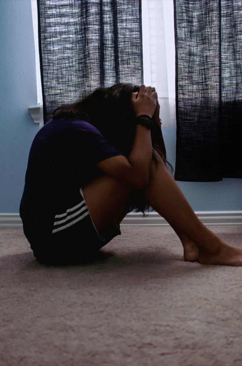 A person sitting by a window with low light, looking down